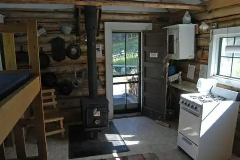 The interior of a rustic cabin featuring a wood-burning stove and a small kitchen area.