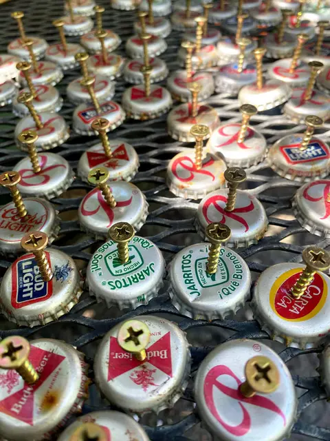 A close-up shot of numerous bottle caps with screws piercing through them on a mesh surface.