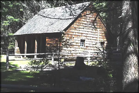 A wooden cabin stands surrounded by trees and a rustic fence.