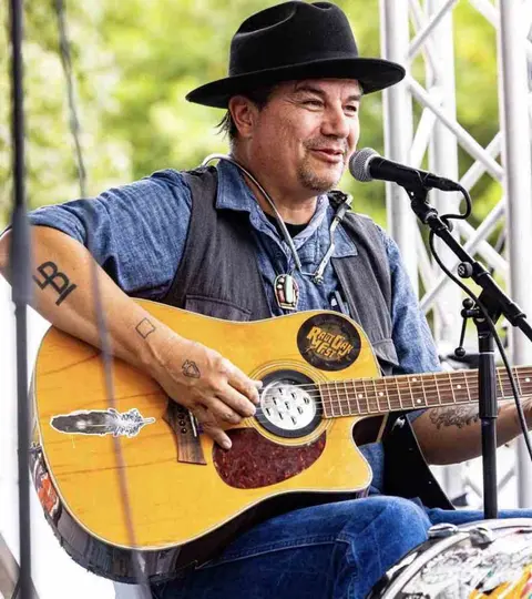 A man plays an acoustic guitar and sings into a microphone.