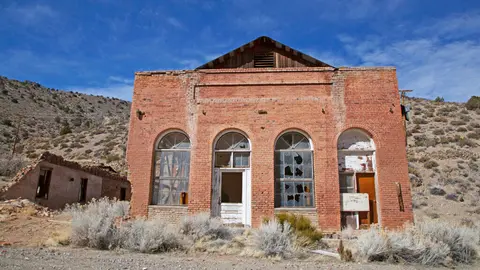 An old brick building stands in an arid landscape with arched windows and a wooden gable.