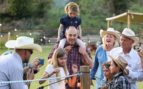 A family and friends gather outside near a ranch fence.