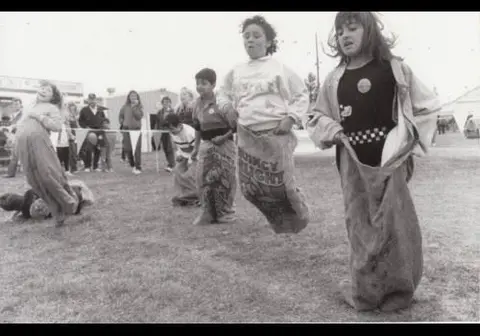 A black and white photograph of children participating in a sack race outdoors.