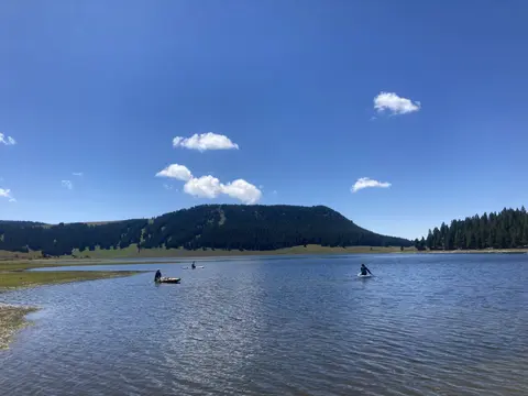 People paddleboarding and kayaking on a lake with a forested hill in the background.