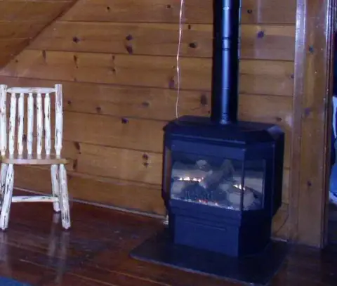 A black stove stands in a wood-paneled interior next to a rustic chair.