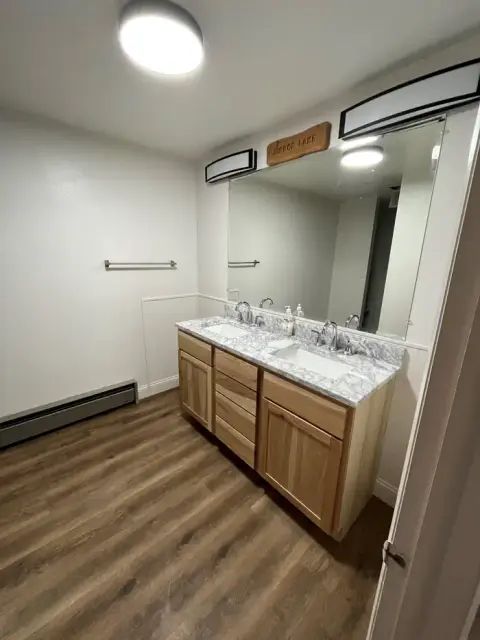 A bright bathroom featuring a double vanity with wooden cabinets and a marble countertop.