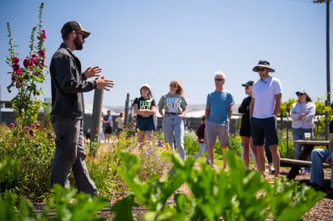 A guide talks to a small group of people in an outdoor garden.