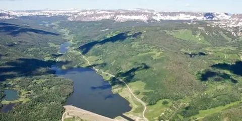 An aerial view of a mountain valley with a lake and distant snow-capped peaks.