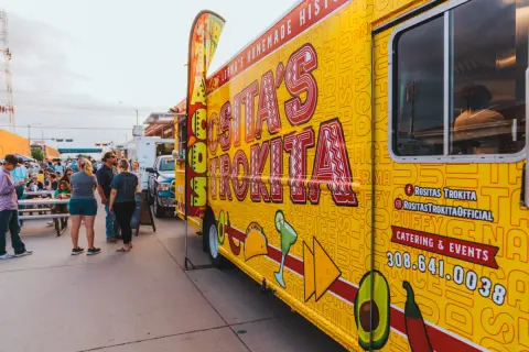 A brightly decorated food truck parked outside with people standing nearby.