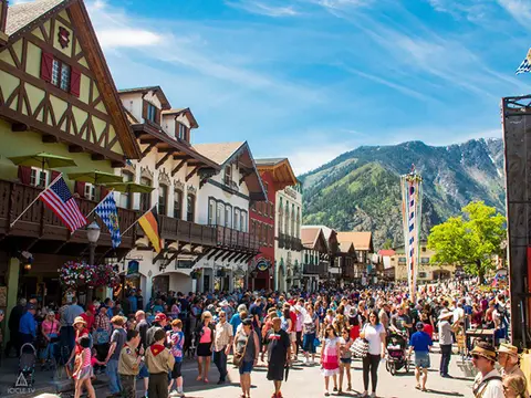 A crowded street in a Bavarian-style mountain town with festive flags.