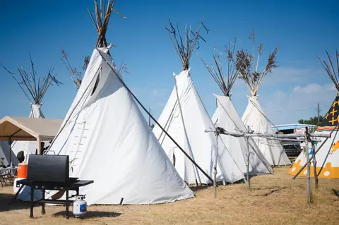 A row of white tipis set up outdoors under a clear blue sky.