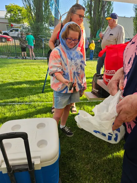 A child in a tie-dye hoodie holding a fish outdoors.