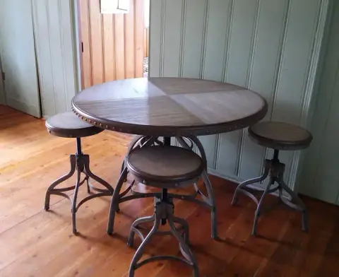 A round wooden table with three matching stools inside a room.