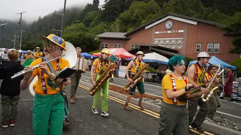 A marching band with yellow shirts and hard hats performs in a street.