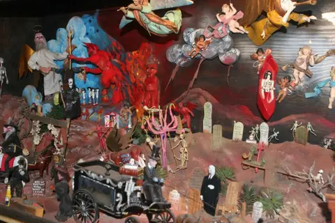 A diorama depicting various figures in a landscape with a carriage, angels, and demons.