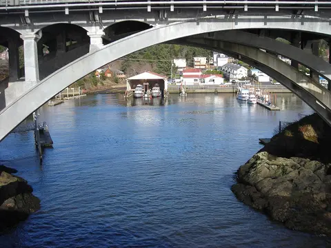 A view of a waterway and harbor buildings framed by the arches of a concrete bridge.