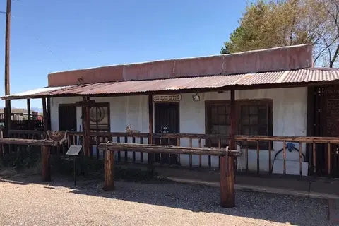 An old single-story building with a porch and a tin roof under a blue sky.