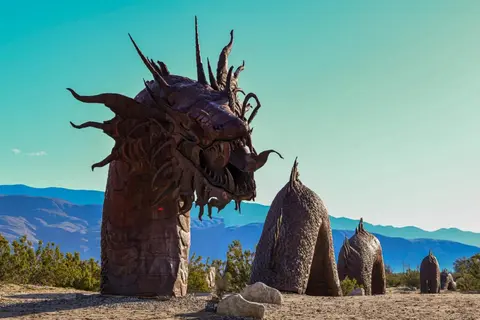 A large metal dragon sculpture stands in a desert landscape.