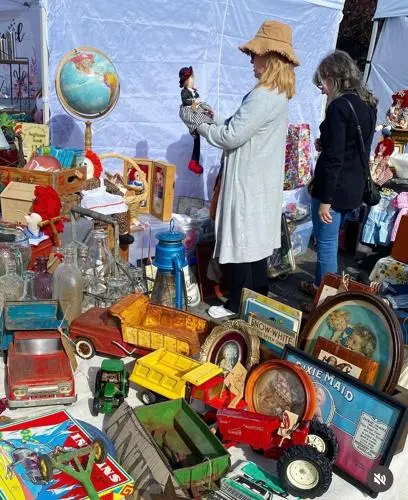 Two women browse items at an outdoor market stall filled with vintage toys and collectibles.