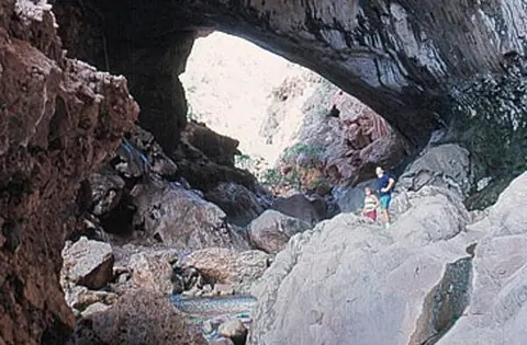 People stand near rocks inside a large natural rock arch or cave.