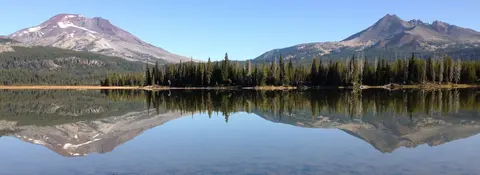 A scenic view of mountains and trees reflected in a calm lake.