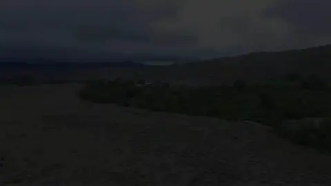 A very dark landscape shows rolling hills under a cloudy sky.