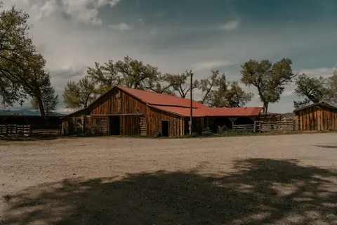 A rustic wooden barn with a red roof stands under a cloudy sky.