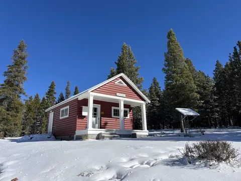 A red and white cabin stands in a snow-covered landscape under a clear blue sky.
