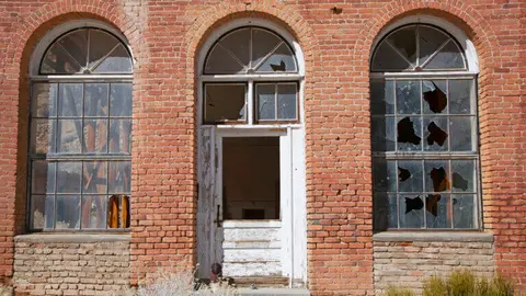 An old brick building exterior featuring arched windows and a weathered doorway with broken glass.