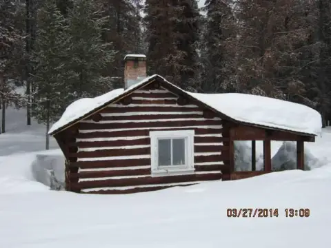 A log cabin covered in deep snow in a forest.