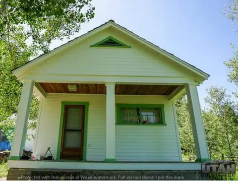 A small light-colored house with a covered porch and green trim.