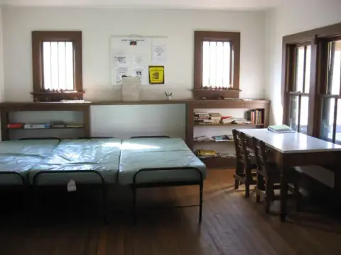 An interior room with multiple metal framed beds and a table with chairs.