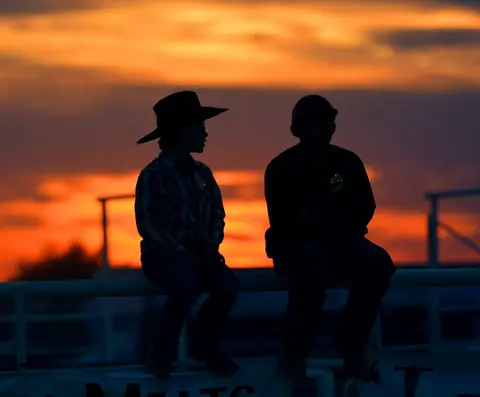 A silhouette of two people sitting on a fence during a sunset.