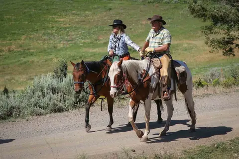 Two people ride horses along a dirt path.