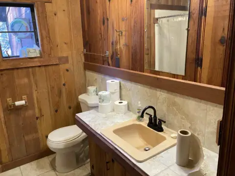A rustic bathroom with wood paneled walls, a tiled vanity, toilet, and sink.