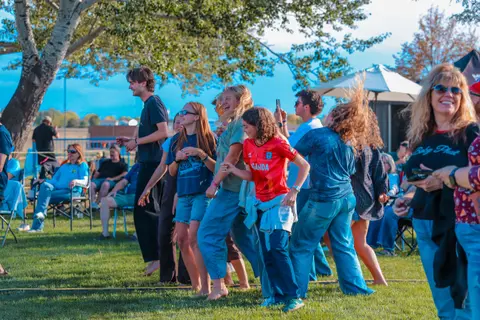 A group of people dancing and enjoying themselves outdoors on a grassy field.