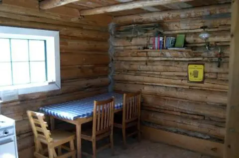 The interior of a rustic log cabin features a dining table with chairs.