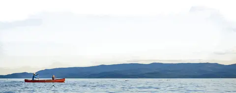 A red canoe on a calm lake with mountains in the background.