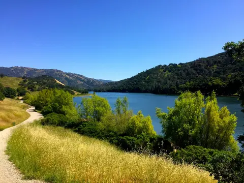 A scenic view of a lake bordered by hills and a trail.
