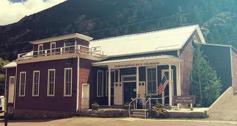 Exterior view of a dark red historic building with a white porch and an American flag.