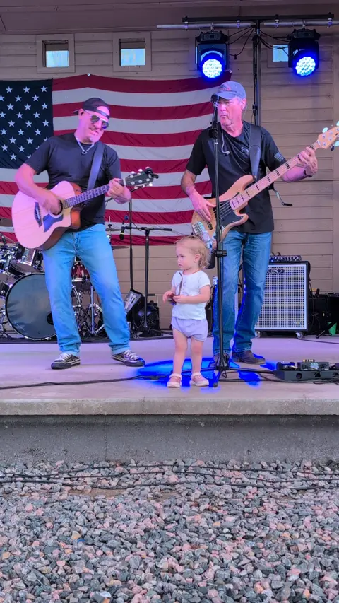 Two musicians perform on stage with a small child standing in front of them.