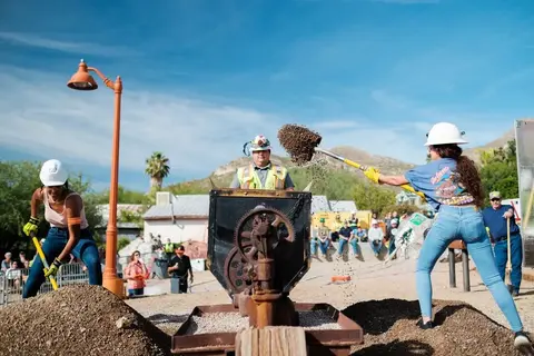 People shoveling dirt into a piece of mining machinery outdoors.