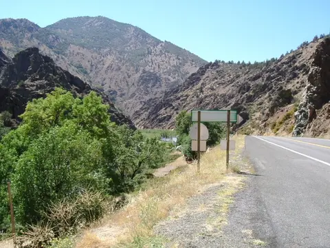 A paved road runs alongside a canyon with mountains in the background.