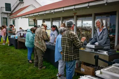 People stand in line at an outdoor food service station.