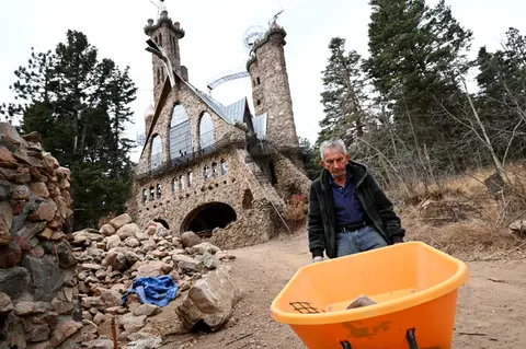 A man works with a wheelbarrow in front of a stone castle.