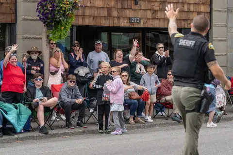 A sheriff waves to a crowd of people watching a parade outside a building.