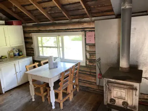 An interior view of a rustic log cabin with a table and a wood-burning stove.