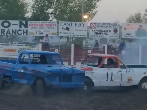 Two pickup trucks in a demolition derby arena.
