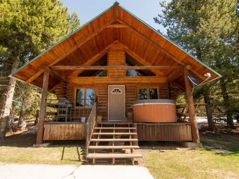 An exterior view of a log cabin with a hot tub on the front porch.