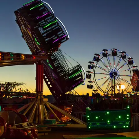 Carnival rides lit up at dusk with a sunset in the background.